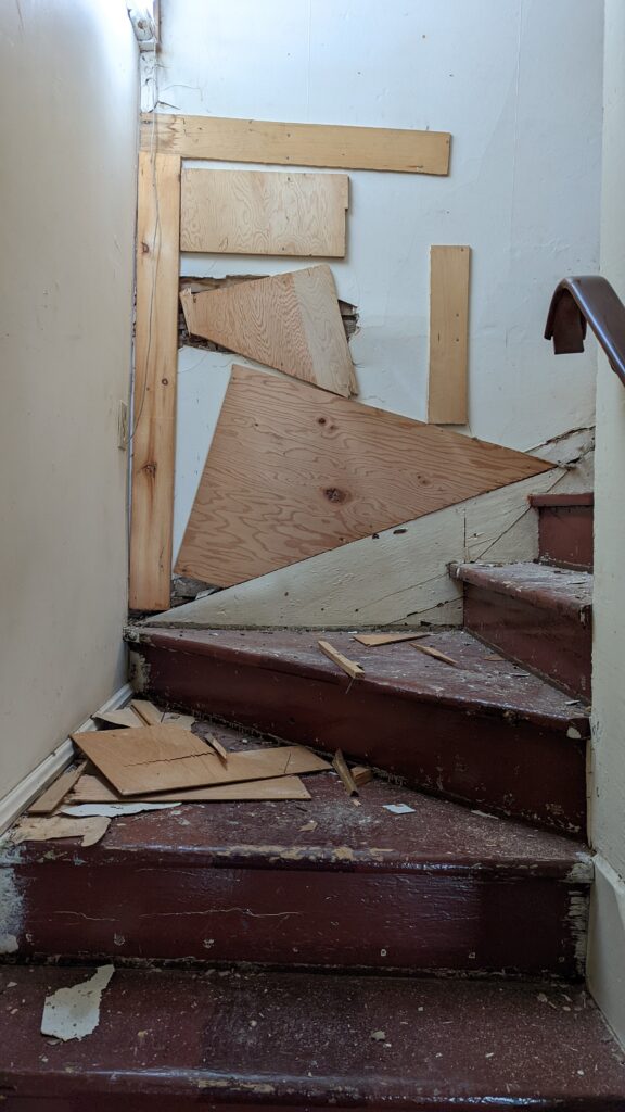 stairwell under renovation with scraps of plywood hiding damaged wall